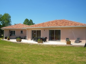 Une maison à deux étages, avec un toit en tuiles, une terrasse dotée de mobilier d’extérieur et une porte-fenêtre coulissante donnant sur un espace abrité.