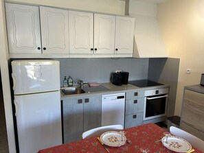 A compact kitchen with white cabinets, a built-in dishwasher, a stove, and a small oven.