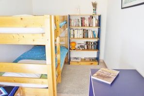 Une chambre avec deux lits superposés, une bibliothèque et une table sur laquelle se trouve un livre.