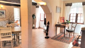 Amplia sala de estar con mesa de comedor, sillas, sofá y mesa de centro. Cuenta con un ventanal con cortinas, un radiador y un tapete en el suelo.