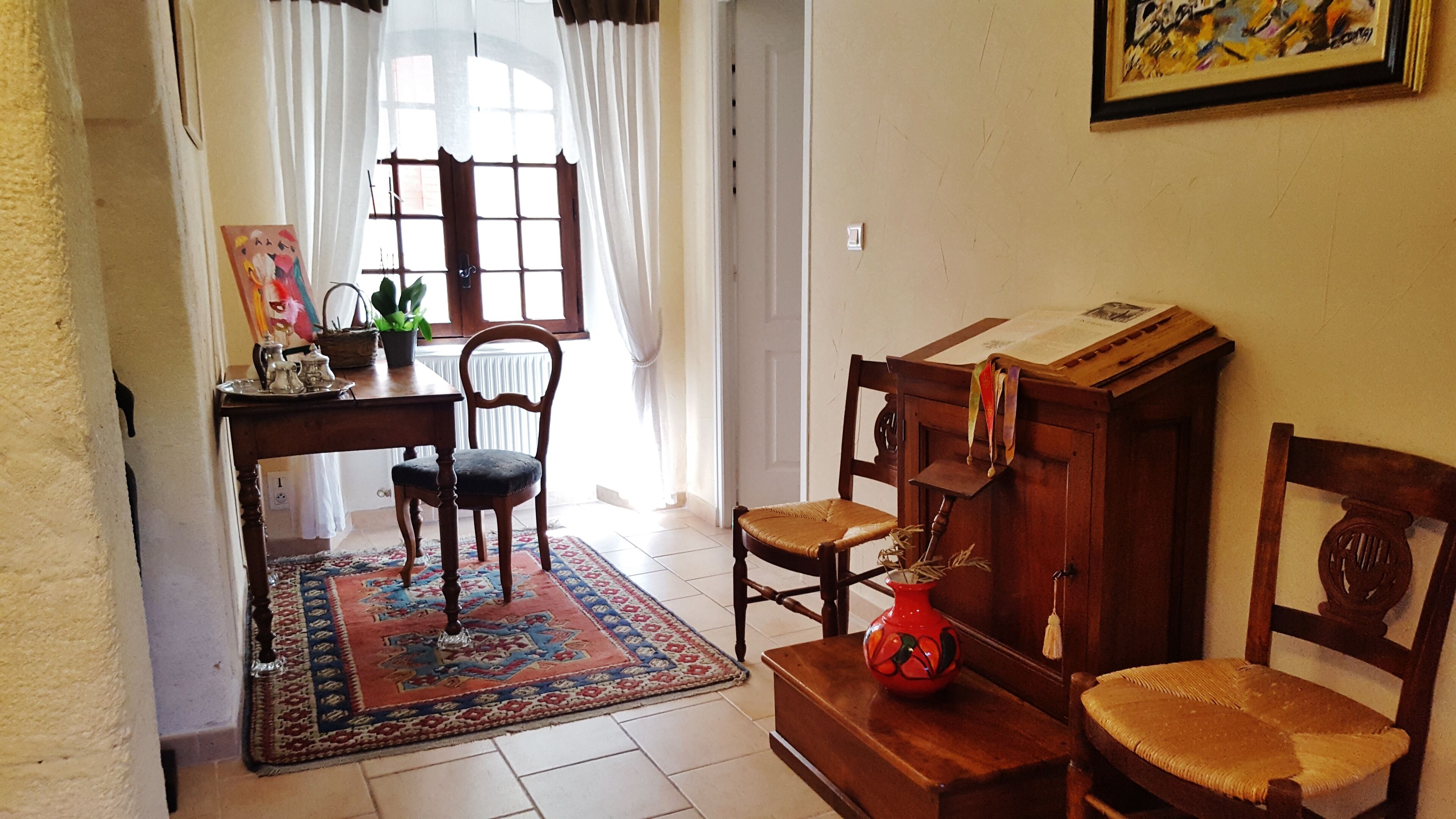 A room with a wooden desk, a chair, a small table with a vase, and a bookshelf.