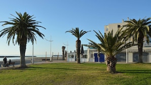A coastal area with palm trees, a bench, and a building with a blue garage door. - Family-Friendly 3-Room Apartment with A/C, WiFi, and Garage, 250m from Beach in Le Grau-du-Roi (Le Grau-du-Roi)