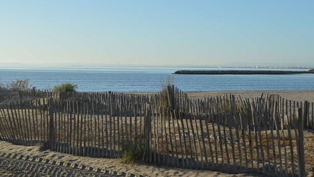 A sandy beach with a wooden fence in the foreground and a calm sea in the background. - Family-Friendly 3-Room Apartment with A/C, WiFi, and Garage, 250m from Beach in Le Grau-du-Roi (Le Grau-du-Roi)