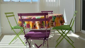 A room with a table covered by a colorful tablecloth, green folding chairs, and a purple cushion. - Family-Friendly 3-Room Apartment with A/C, WiFi, and Garage, 250m from Beach in Le Grau-du-Roi (Le Grau-du-Roi)
