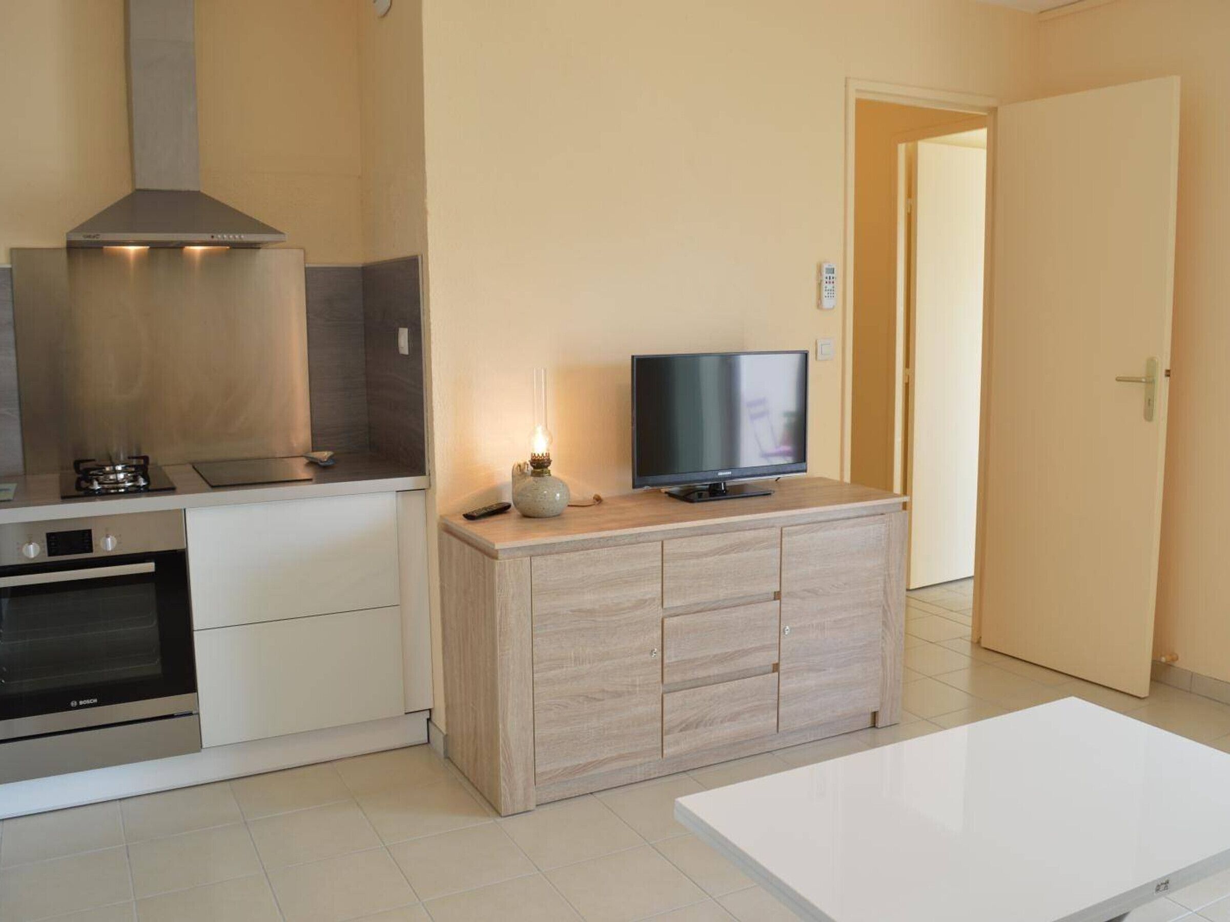 A modern kitchen with a Bosch oven, a stove, and a TV on a wooden cabinet.