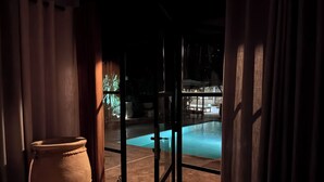 A view through a glass door leading to a swimming pool area at night. - Casbah d'architecte,Chic et Luxe, 305 comments 5*,Optional meals and massages (Essaouira)