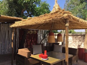 An outdoor seating area with a thatched roof, wooden furniture, and a table with red cups.