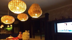 A dimly lit room with a wooden table, wicker lamps, and a television displaying a news channel. - Casbah d'architecte,Chic et Luxe, 305 comments 5*,Optional meals and massages (Essaouira)