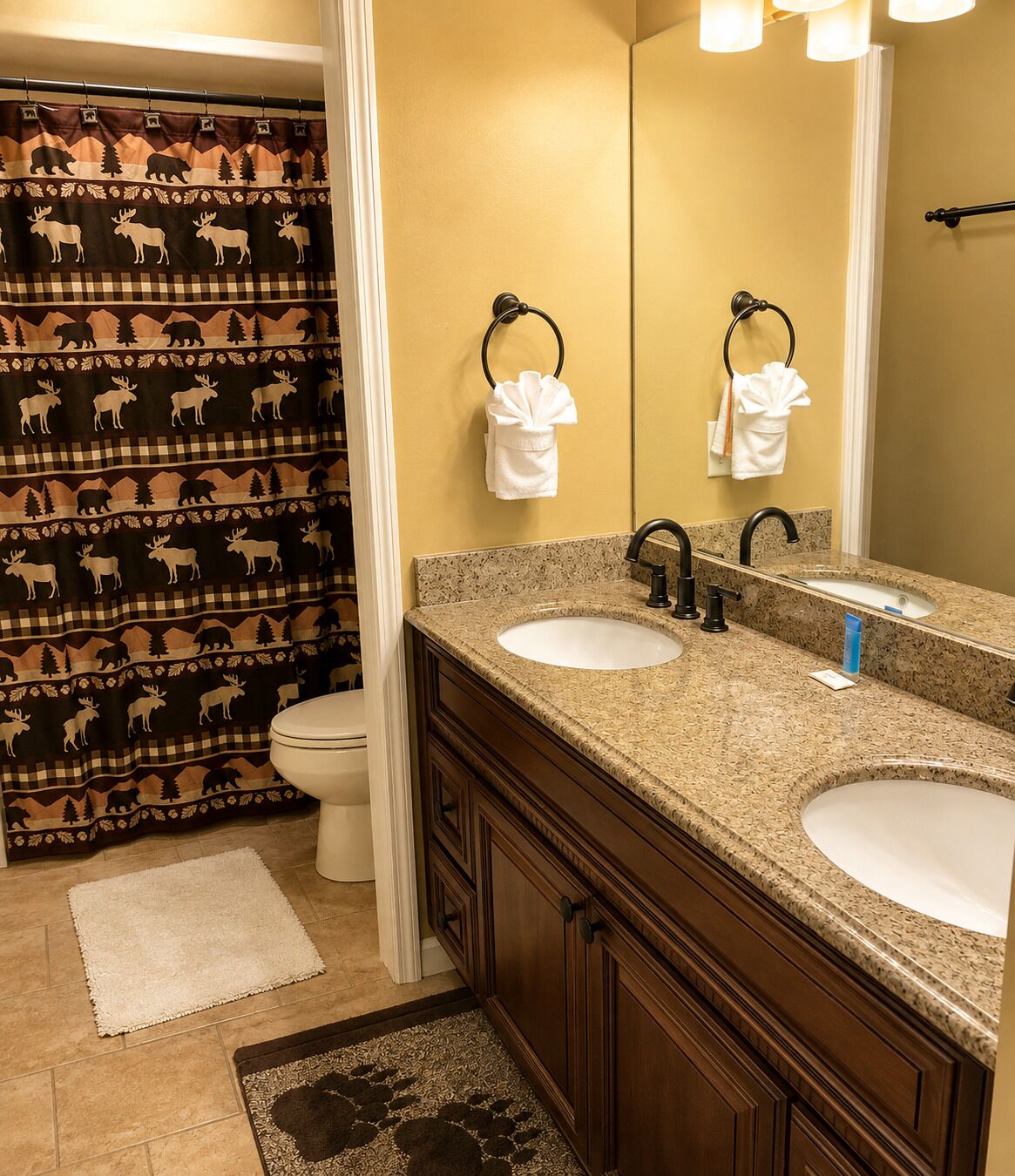 Une salle de bain avec un double lavabo, des toilettes et un rideau de douche à motifs animaliers.
