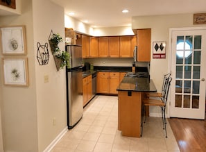 A kitchen with wooden cabinets, a stainless steel refrigerator, a sink, and a stove. There is a door with a sign that reads 'Experts Only' and a framed picture on the wall.