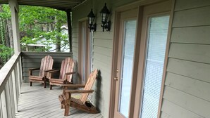 A covered porch with wooden chairs and a bench, a door with a window, and a wall-mounted lantern. - Gatlinburg Cabin 4BR 2.5BA Hot Tub 7 Beds Low Cleaning Fee Smoky Mountains Dolly (Gatlinburg)
