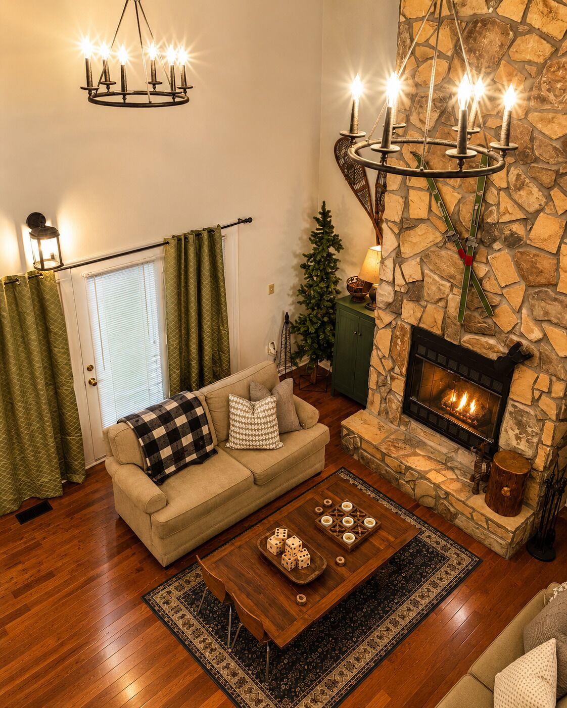 Un salon chaleureux avec une cheminée en pierre, une table basse en bois sur laquelle sont posés des dés, un canapé agrémenté de coussins à motifs et un luminaire suspendu.