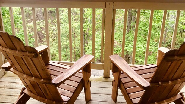Two wooden Adirondack chairs on a wooden deck with a white railing, overlooking a forested area. - Gatlinburg Cabin 4BR 2.5BA Hot Tub 7 Beds Low Cleaning Fee Smoky Mountains Dolly (Gatlinburg)