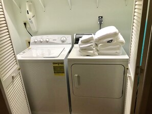 A laundry room with a front-loading washer and dryer, a stack of folded towels, and an ENERGY GUIDE sticker on the washer.