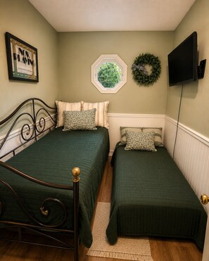 A bedroom with two beds, a window, a television, and a framed picture on the wall.