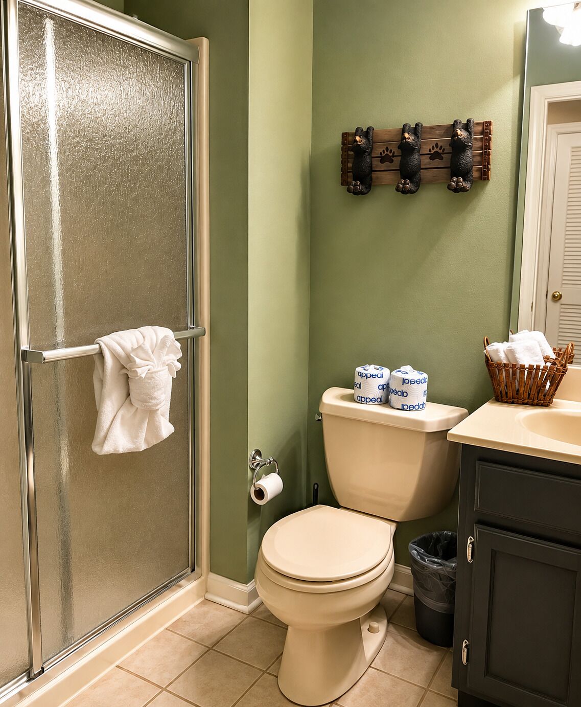 Un baño con cabina de ducha de vidrio, un inodoro con papel higiénico y una cesta de toallas en el mostrador.