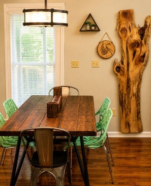 A dining area with a wooden table, chairs, a hanging light fixture, and a large wooden sculpture on the wall.