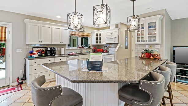 A modern kitchen with white cabinets, a large island with bar stools, and pendant lighting. -  VACAY TIME:HHI Retreat: Pool/Hot Tub/Near Beach, Pets, Last Minute Rentals Now! (Hilton Head Island)