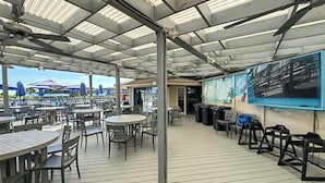 Eine Terrassengaststätte mit Tischen und Stühlen, einem Wandgemälde und Blick auf das Meer.