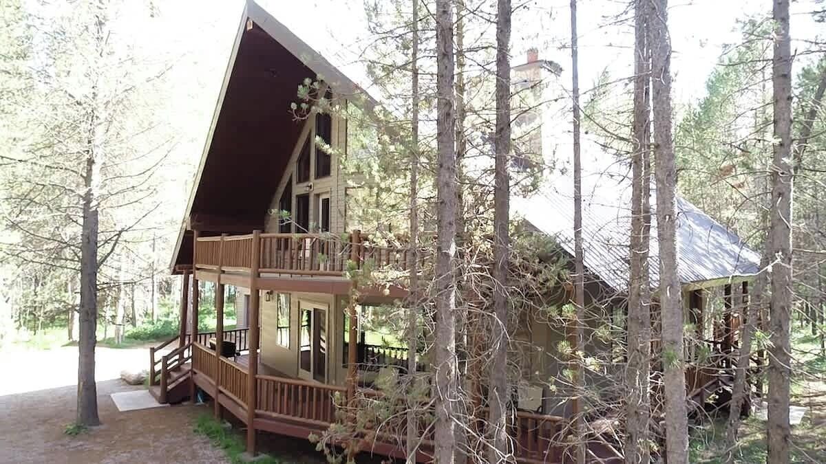 Eine zweigeschossige Holzhütte mit einem Balkon, umgeben von Bäumen.