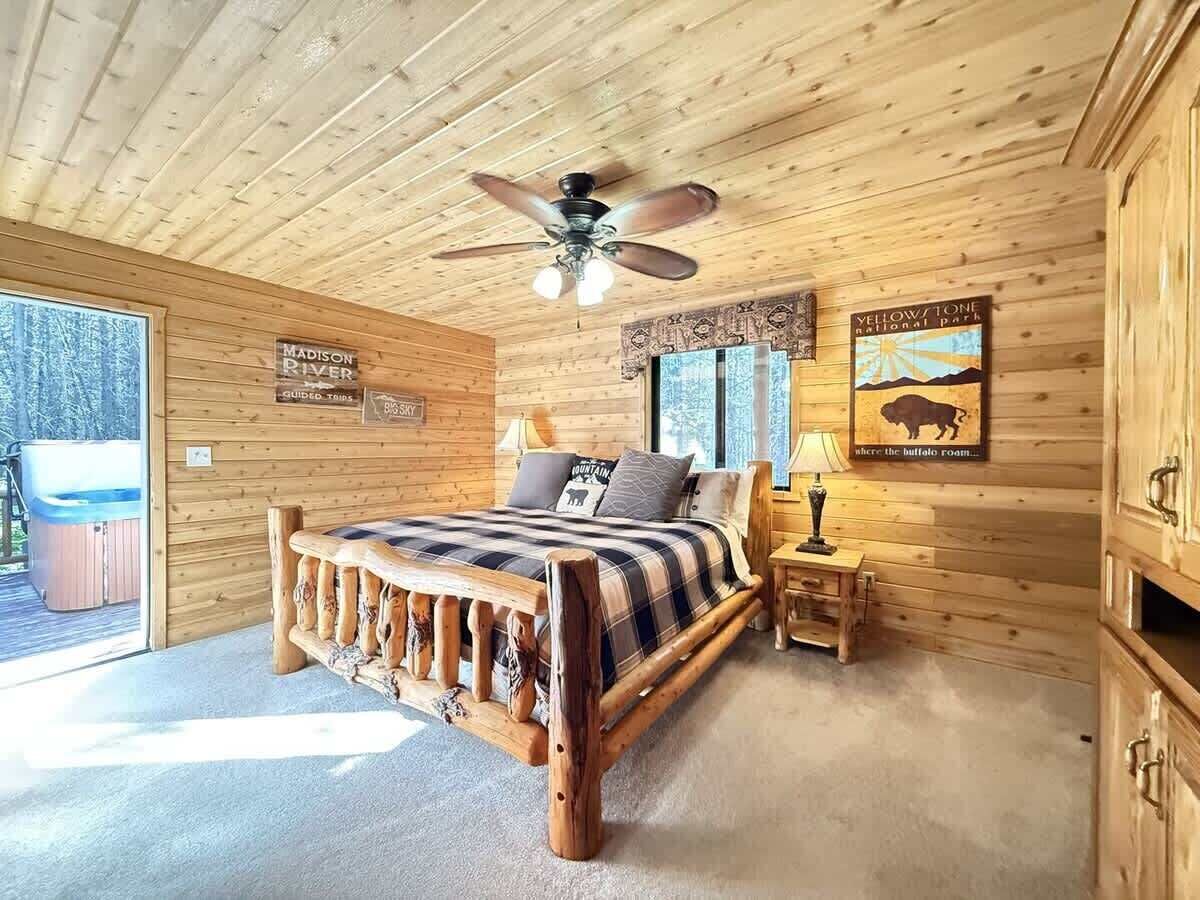A wooden cabin bedroom with a bed, a ceiling fan, a nightstand, and a sign for Yellowstone National Park.