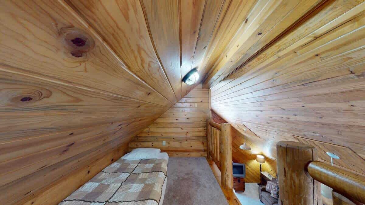 A cozy wooden cabin room with a bed, a small table, and a lamp.