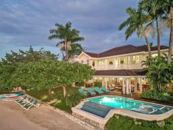 A large house with a swimming pool, lounge chairs, and palm trees. - Beachfront Villa, Staff, Boat, Pool, Tennis, Gated (Montego Bay)