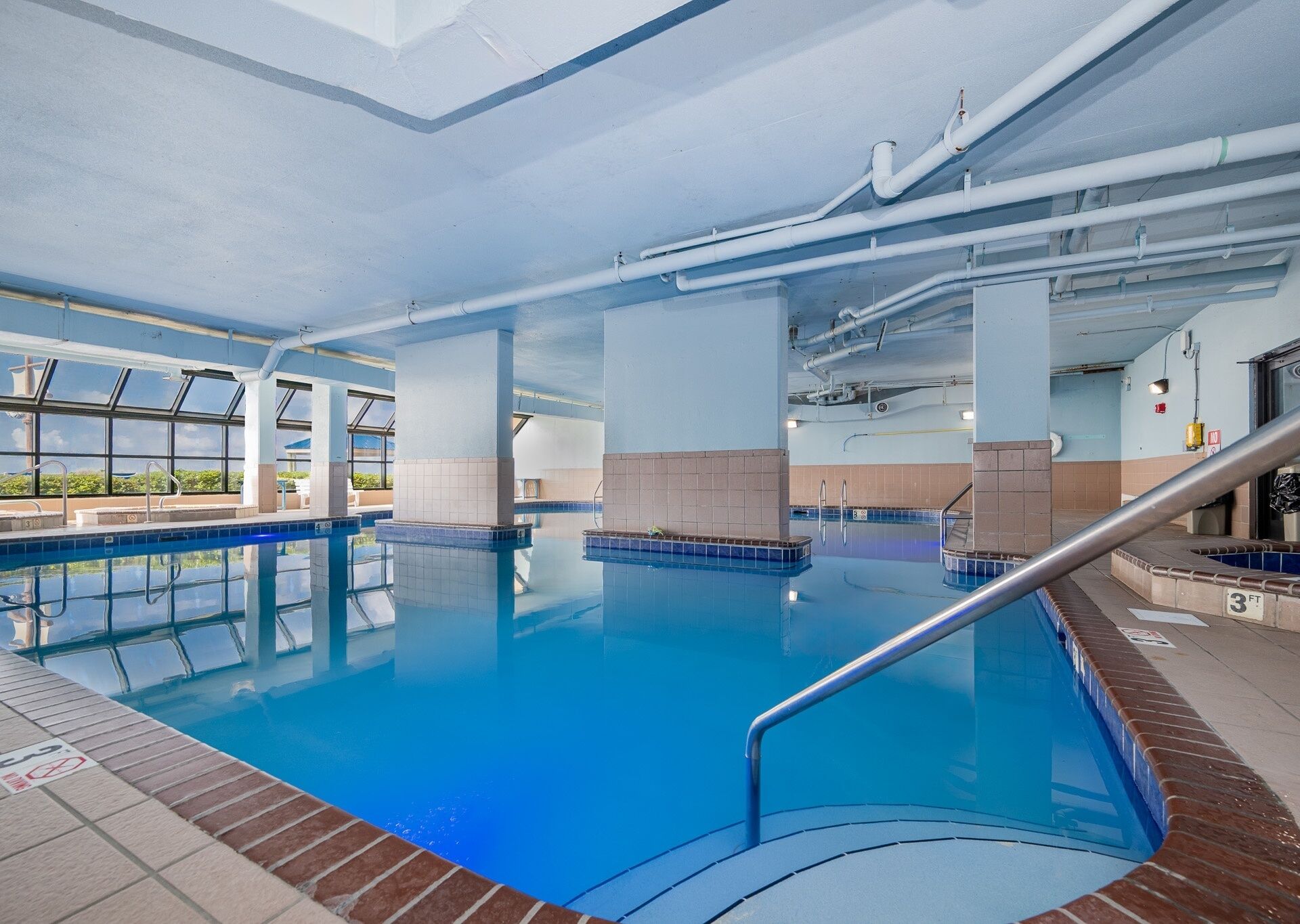 An indoor swimming pool with clear blue water, tiled walls, and a visible ceiling with pipes.