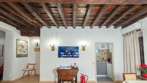 Una habitación con techo de madera, una mesa de comedor con sillas, un televisor en la pared y una cocina visible a través de un vano abierto.