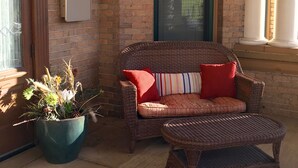 A wicker chair with red and striped cushions, a potted plant, and a brick wall with a green door.