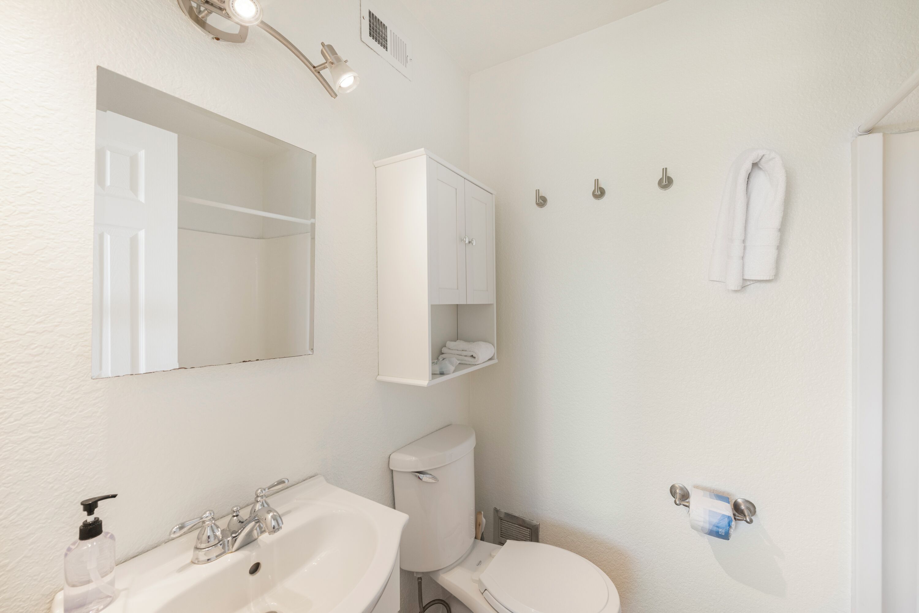 A bathroom with a sink, toilet, mirror, and towel rack.