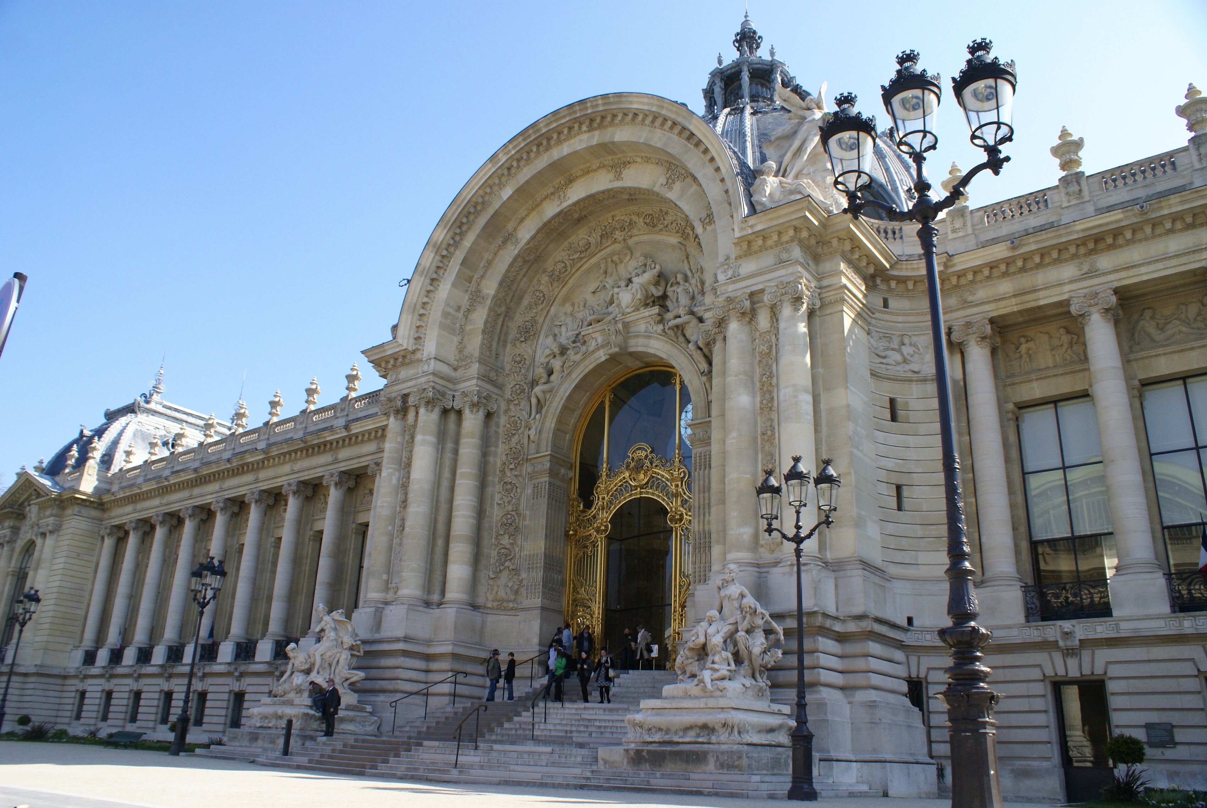 A grand building with ornate architecture, large steps leading to a golden entrance, and classical statues.