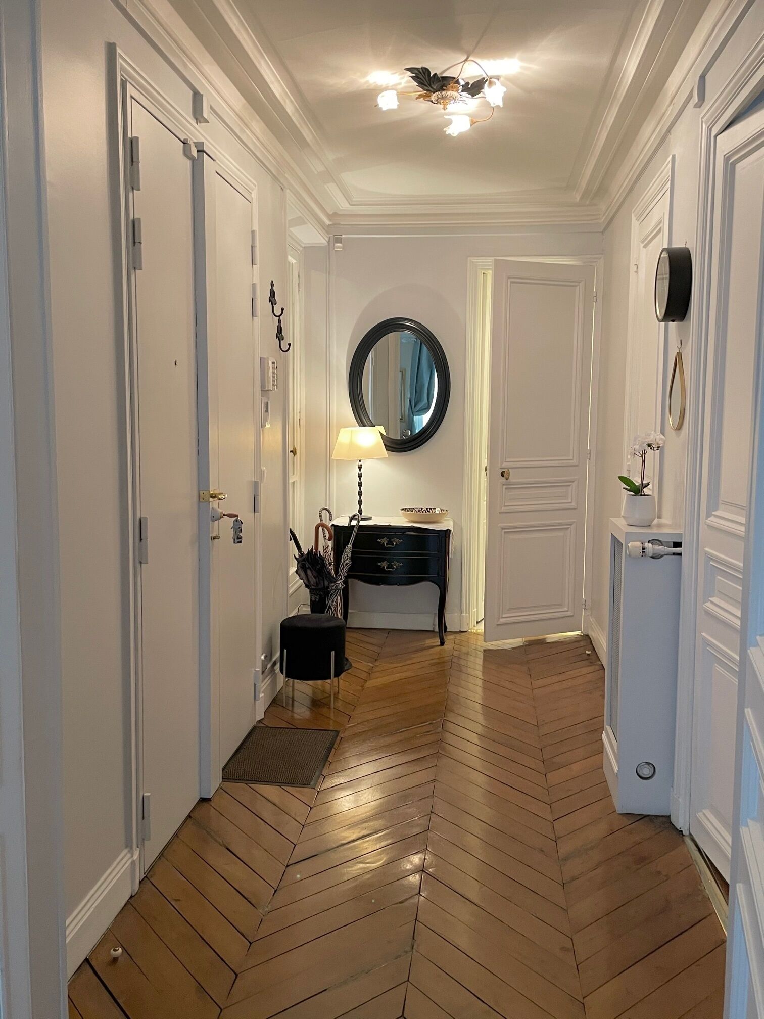 A hallway with wooden flooring, white doors, a black console table with a lamp, and a round mirror on the wall.