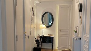 A hallway with wooden flooring, white doors, a black console table with a lamp, and a round mirror on the wall. - Ideal for family, friends, 2 bedrooms, 2 BR, 2 WC, 5 mn walk from Champs-Elysées (Paris)
