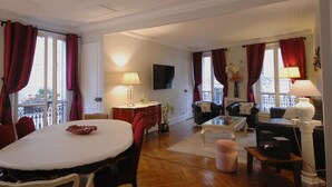A spacious living room with a dining area, furnished with a table, chairs, sofas, and lamps. - Ideal for family, friends, 2 bedrooms, 2 BR, 2 WC, 5 mn walk from Champs-Elysées (Paris)
