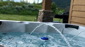 Un jacuzzi con agua brotando de un caño, rodeado por una terraza de madera y un pilar de piedra.