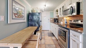 Une cuisine avec des meubles blancs, un réfrigérateur noir, une table en bois et un chien.