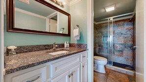 Une salle de bain dotée d’un comptoir en granit, d’un grand miroir, de toilettes blanches et d’une douche à parois de verre.