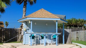 Un petit bâtiment d’un seul étage, à la façade bleue et au toit recouvert de tuiles, doté d’un patio abrité avec une table et des chaises.