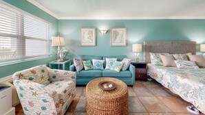 Une pièce aux murs de couleur turquoise, avec un canapé bleu, un pouf en osier et un lit recouvert d’une couvre-lit à motifs.