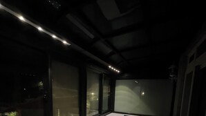 A dimly lit room with a long table, two chairs, a sofa, and large windows.