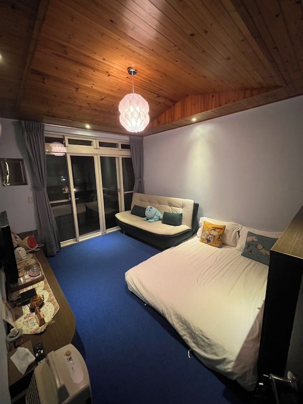 Un dormitorio con cama, sofá, escritorio, silla, calefactor y ventana con cortinas.
