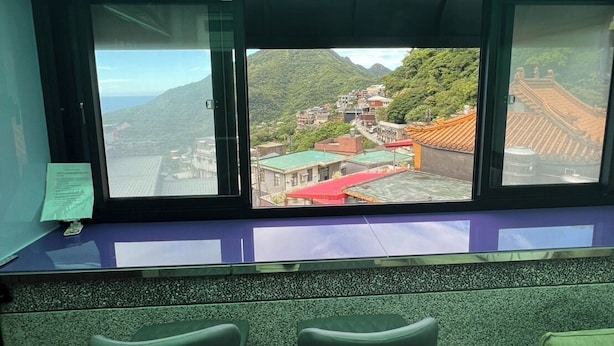 A room with a large window overlooking a mountainous landscape, two chairs, and a wooden floor.