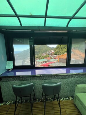 Una habitación con un amplio ventanal que da a un paisaje montañoso, dos sillas y suelo de madera.