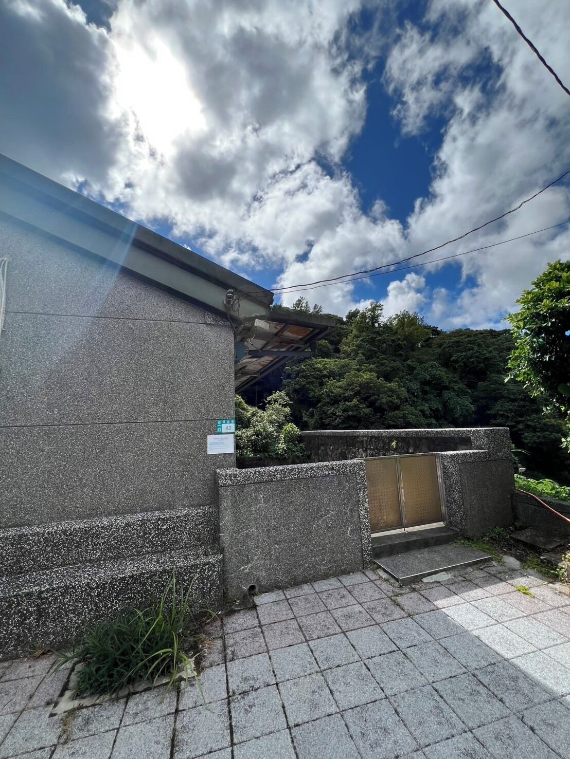 Un edificio con fachada de piedra, una reja metálica y un área de acceso pavimentada.