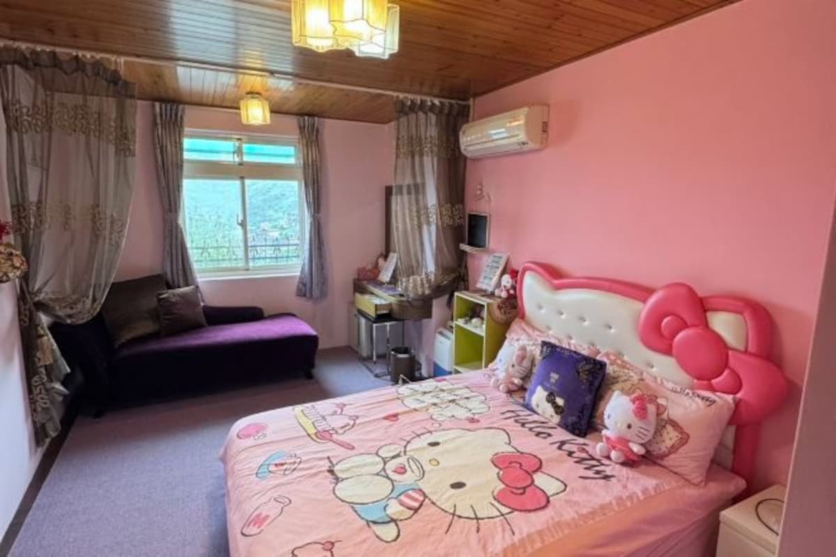 Un dormitorio rosa con una cama decorada con diseño de Hello Kitty, un sofá morado y un escritorio con una computadora.