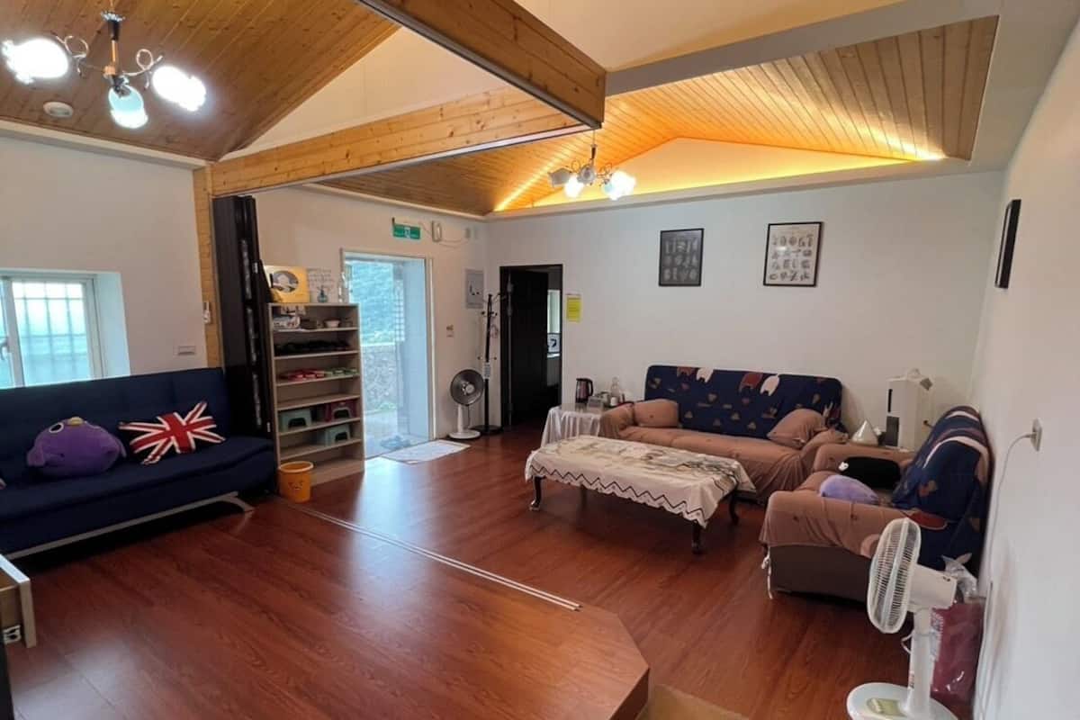 A spacious room with wooden flooring, a sofa, a bed, and a fan.