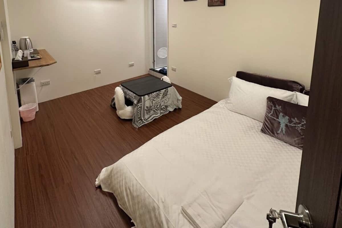 A bedroom with a bed, a small table, a chair, a wardrobe, and a wall-mounted air conditioner.