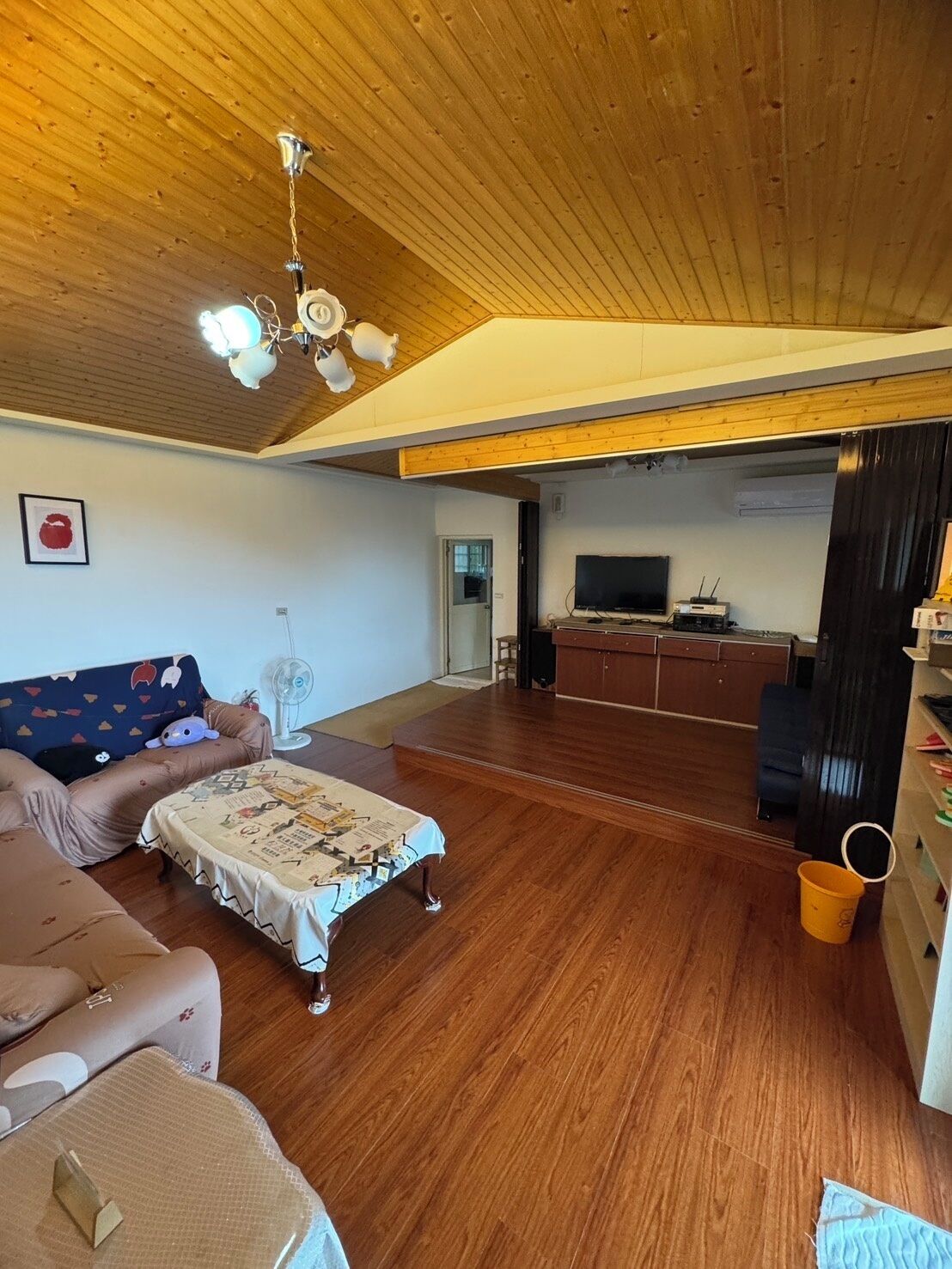 A spacious living room with a wooden ceiling, a sofa, a coffee table, and a television in the background.
