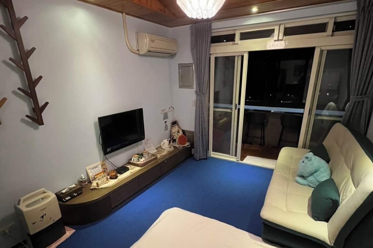 A hotel room with a bed, a sofa, a TV, and a balcony with a view.
